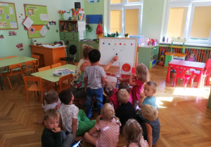 Na zdjęciu dzieci oglądają tablicę, ba której nauczyciel pokazuje czarną kropkę, jako element różnych rysunków.